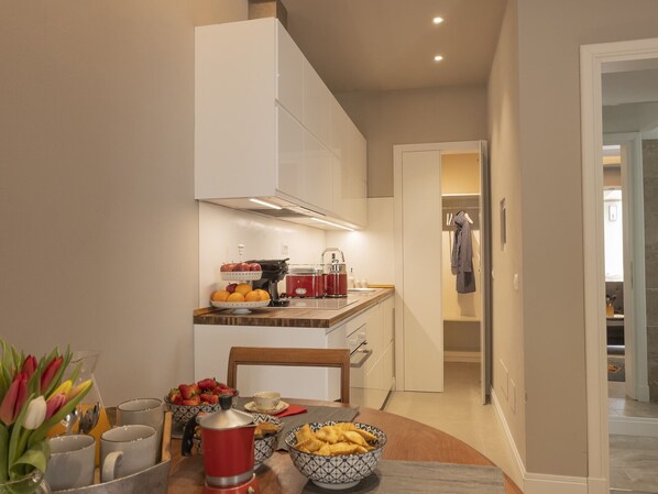 A modern kitchen with white cabinets, a coffee machine, and a dining area with a table set for two. - Il Poggio, an exclusive location with parking (Firenze)