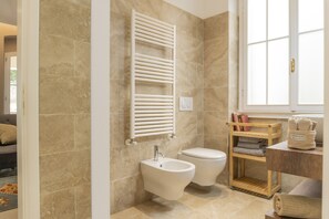 A bathroom with beige tiles, a bidet, a toilet, a towel rack, and a window. - Il Poggio, an exclusive location with parking (Firenze)