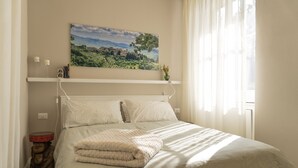 A neatly made bed with a striped bedspread, a white headboard, and a painting of a landscape above it. - Il Poggio, an exclusive location with parking (Firenze)