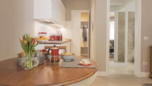 A modern kitchen with white cabinets, a red kettle, and a fruit bowl. A wooden table with a vase of tulips and a teapot is visible. - Il Poggio, an exclusive location with parking (Firenze)