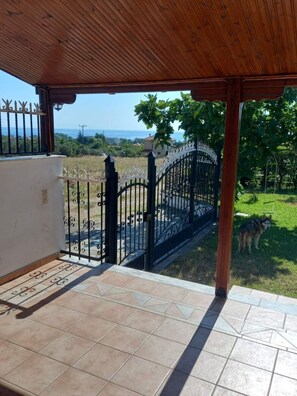 A covered patio with a view of the sea and a fenced garden area.