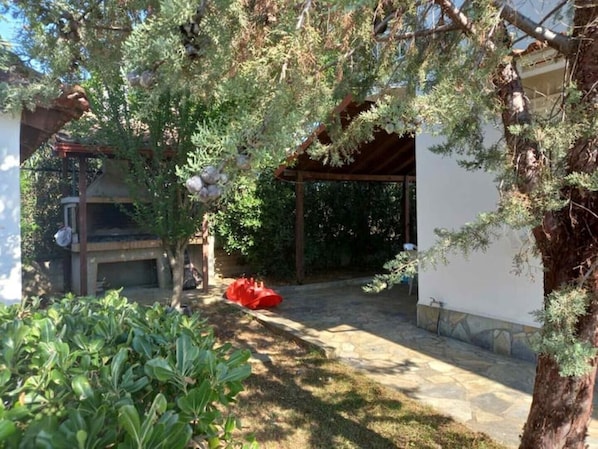 A covered outdoor area with a barbecue grill, a red bean bag, and a stone pathway.