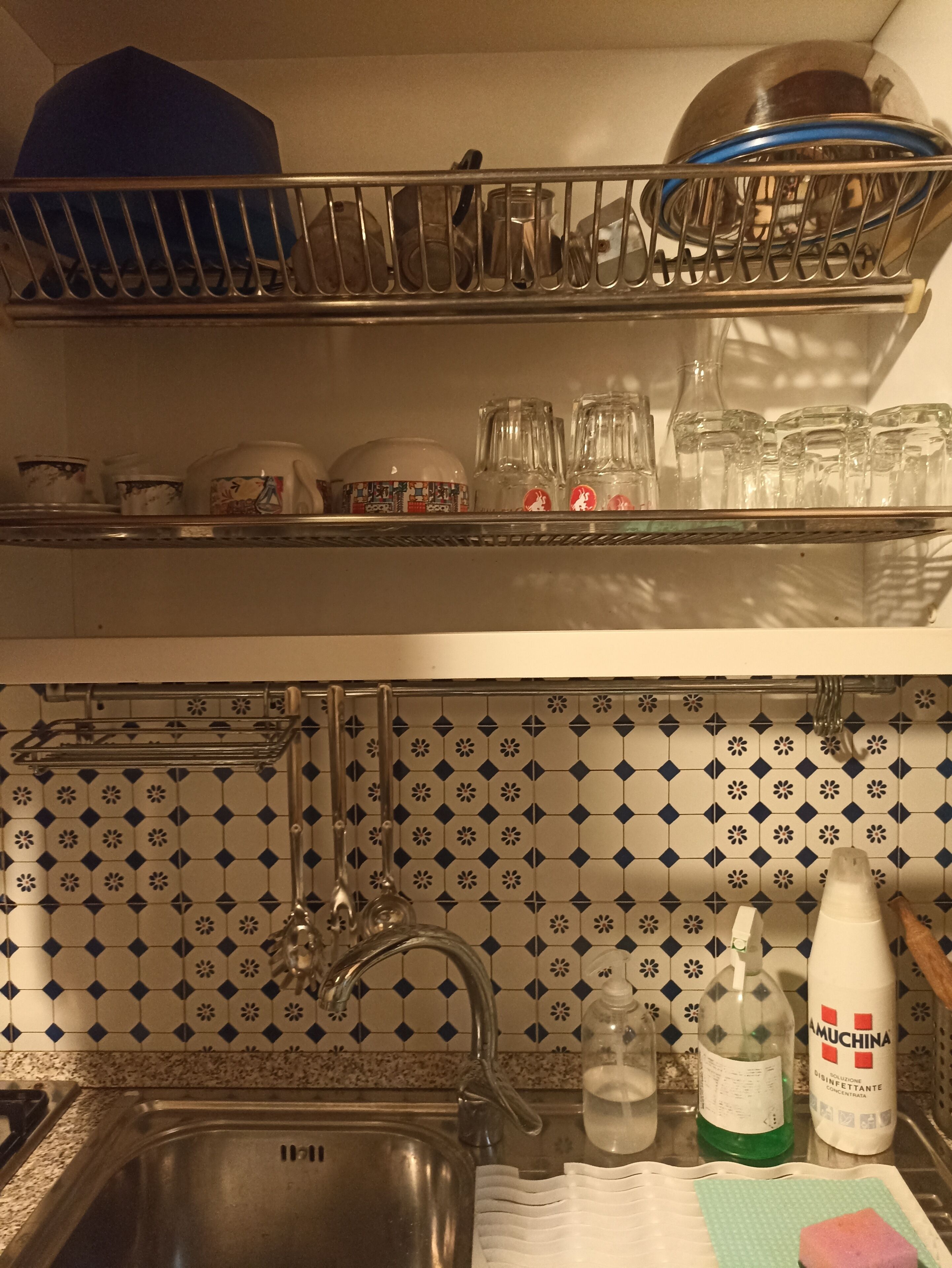 Una cocina con un lavaplatos, un escurreplatos y diferentes utensilios de cocina.