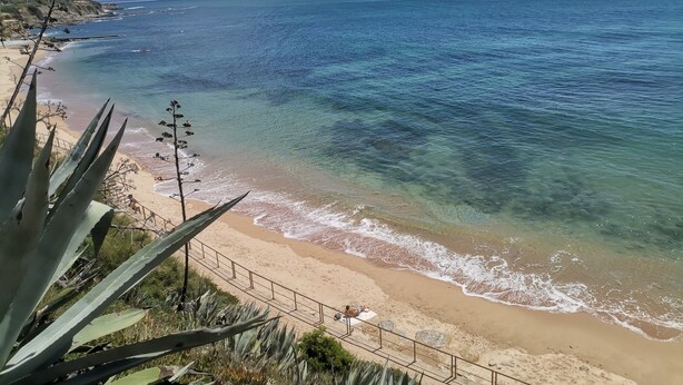 Ein Küstenstrand mit klarem Wasser, Sandstrand und einer Geländer.