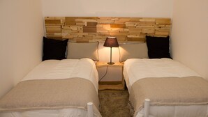 Ein Schlafzimmer mit zwei Betten, einem Holz-Kopfstück, einer Nachttischlampe und Teppichboden.
