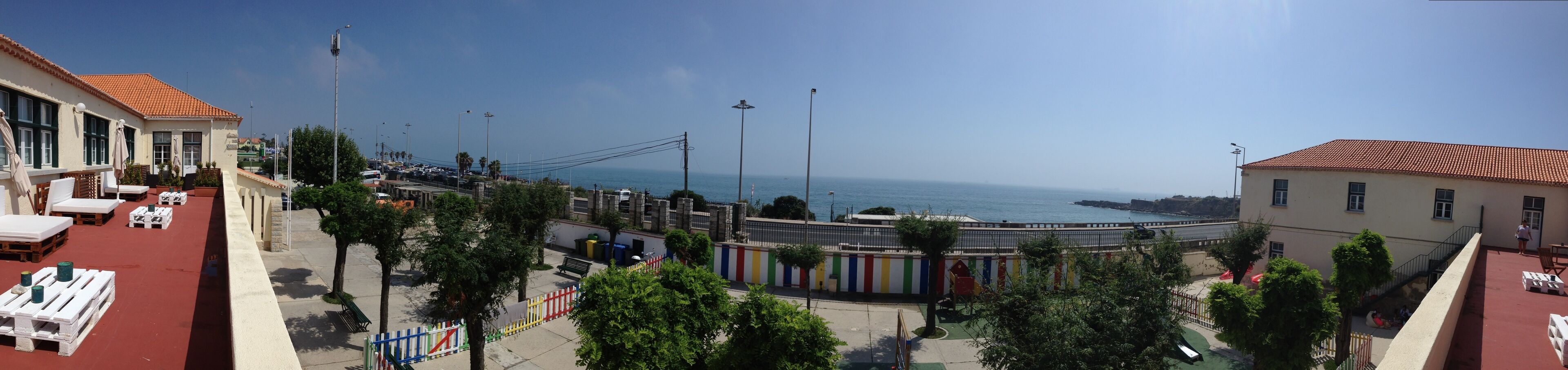 A coastal view with a paved area, benches, and a fence with colorful flags.