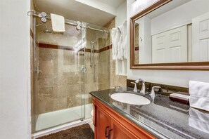 Een badkamer met een douche met glazen wand, een wastafel met een marmeren blad en een spiegel boven de wastafel.