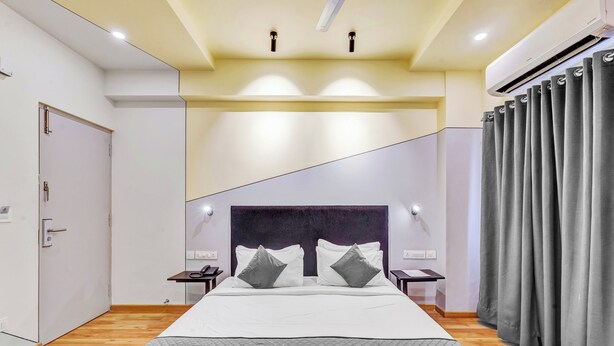 A modern hotel room with a large bed, a headboard, bedside tables, and a window with curtains.