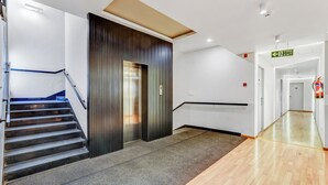 A modern hotel lobby with a staircase, elevator, and a fire exit sign.