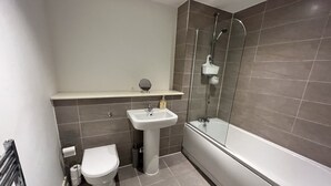 Un baño moderno con inodoro, lavamanos y ducha con mampara de vidrio.