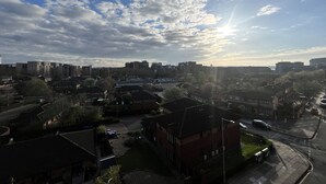 Un barrio residencial con edificios de apartamentos y casas, un cielo despejado con algunas nubes y el sol visible.