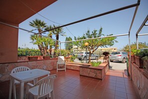 A patio with a white table and chairs, stone walls, and a view of parked cars and trees. - Villetta Santa Lucia by Wonderful Italy (Cefalù)