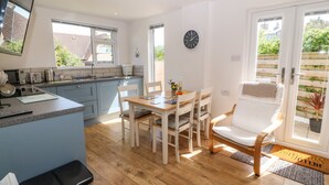 A modern kitchen with a dining area, wooden flooring, and a view of the outside. - Croeso (Holyhead)