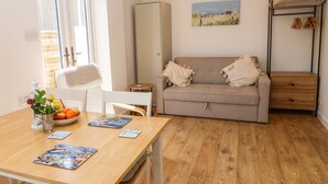 A cozy room with a wooden floor, a grey sofa with cushions, a small table with a vase of flowers, and a painting on the wall. - Croeso (Holyhead)