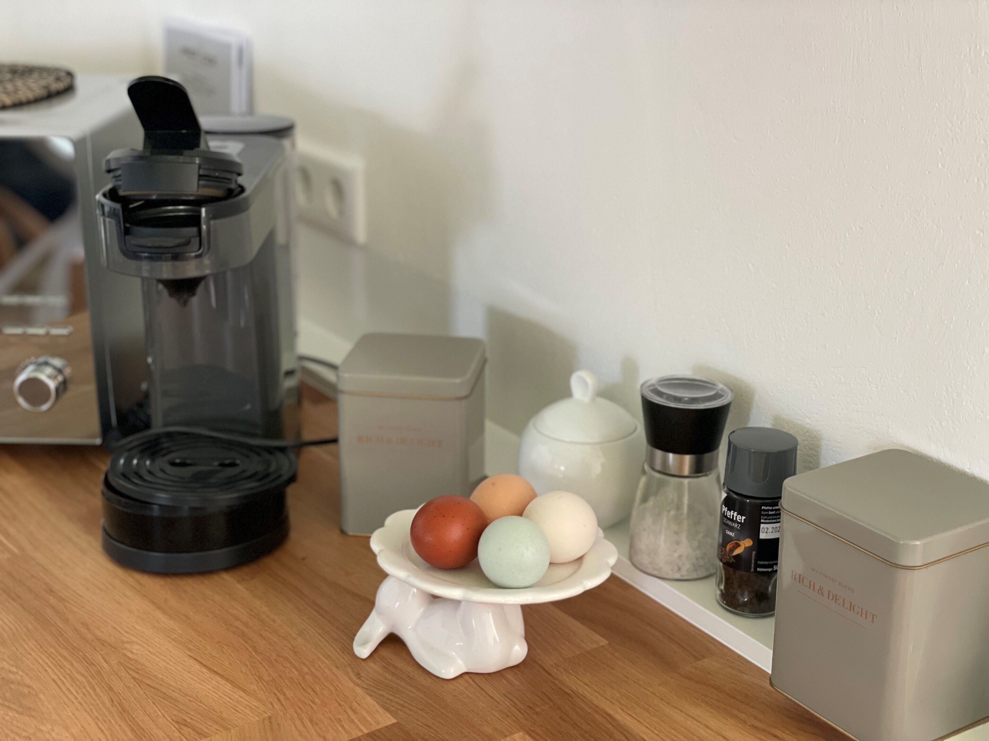 A kitchen counter with a coffee maker, a tea kettle, a sugar container, a salt shaker, and a spice jar.