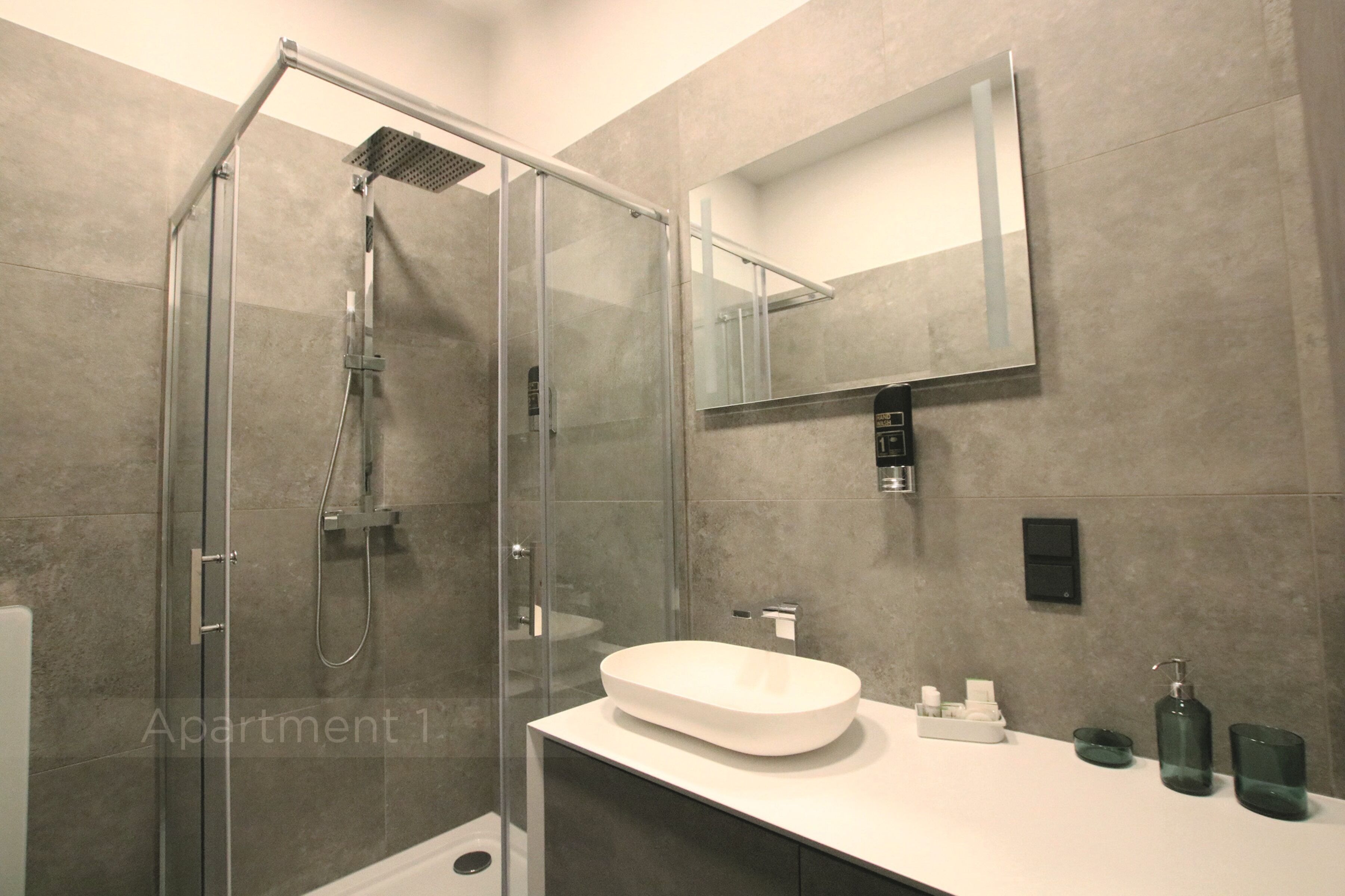 Een moderne badkamer met een douche in een glazen cabine, een witte wastafel en een spiegel erboven.