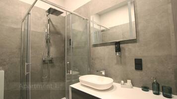 Een moderne badkamer met een douche in een glazen cabine, een witte wastafel en een spiegel erboven.