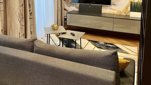 A modern living room with a large flat-screen TV, a sofa, a coffee table, and a lamp. - Street Living Hotel (Vienna)