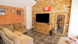 Ein Wohnzimmer mit Backsteinwand, einem großen Flachbildfernseher, einer Holzkommode und einem Sofa.