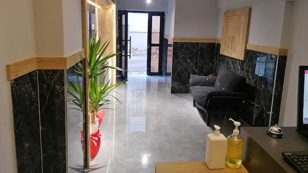 A hotel lobby with a reception desk, a sofa, a potted plant, and a view of the outside. - Esas Pansiyon (Gemlik)