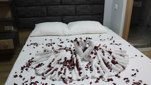 A neatly made bed with white linens and a towel arranged in a fan shape, surrounded by scattered rose petals. - Esas Pansiyon (Gemlik)