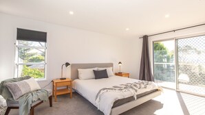 A bedroom with a large bed, two bedside tables, a chair, a window, and a view of the outdoors.