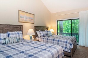 A room with two beds, a painting, a window with a view of trees, and a balcony.