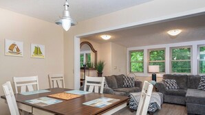 A dining area with a wooden table and chairs, a gray sofa, and a window with a view of trees. - Fairway Villa 1103 at Rumbling Bald (Lake Lure)