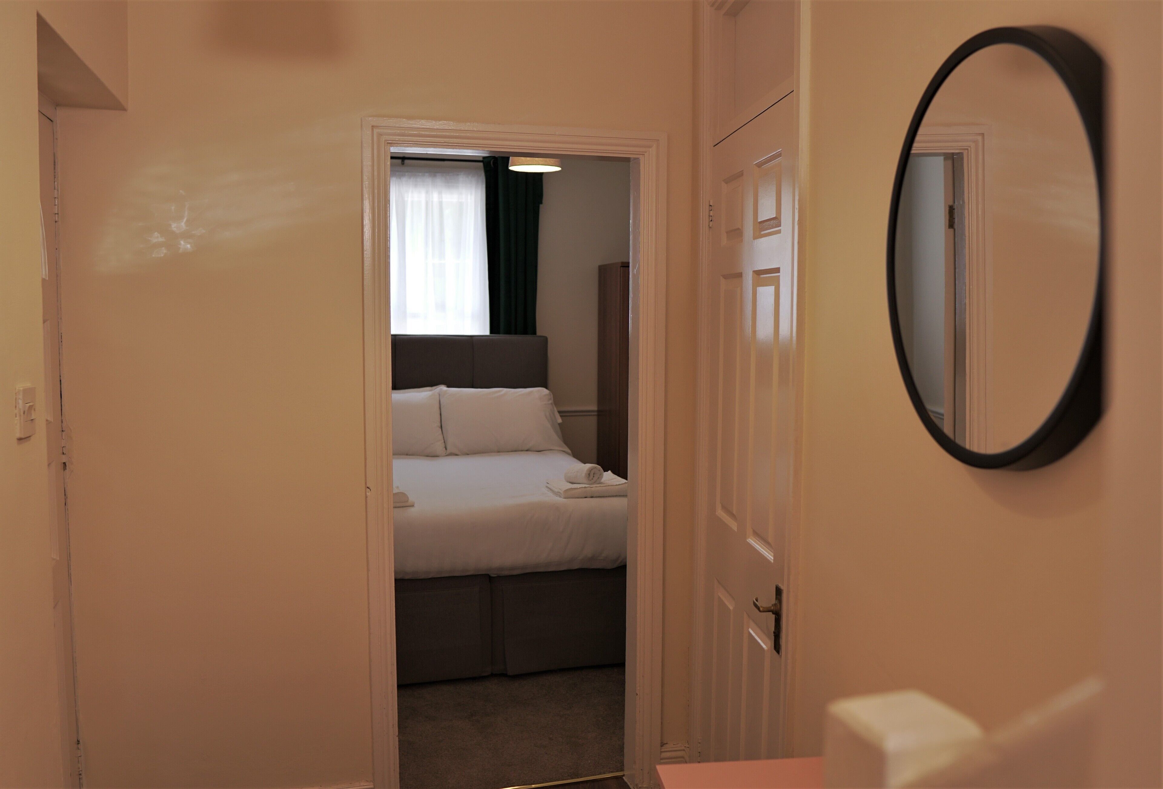 A hotel room with a bed, a bedside table, a mirror, and a door leading to another room.