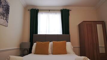 A bedroom with a bed, a nightstand, a lamp, a wardrobe, and a window with curtains.