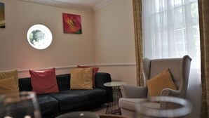 A living room with a dark sofa, a light armchair, a round table, and a painting on the wall. - Meadow Terrace (Shrewsbury)