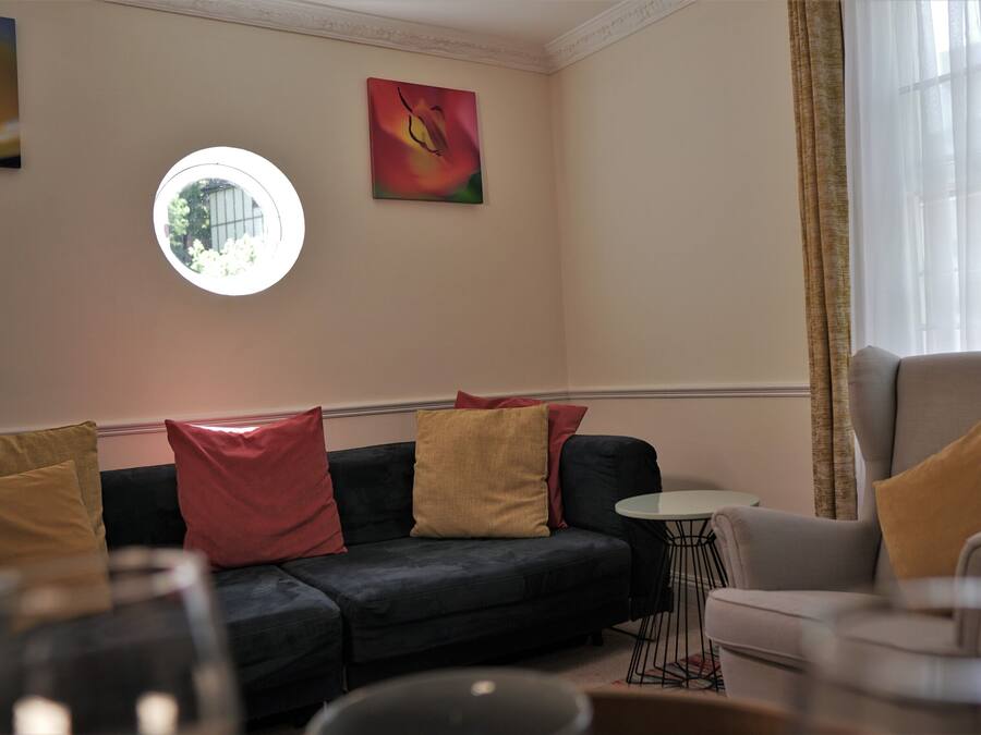 A living room with a dark sofa, a light armchair, a round table, and a painting on the wall.
