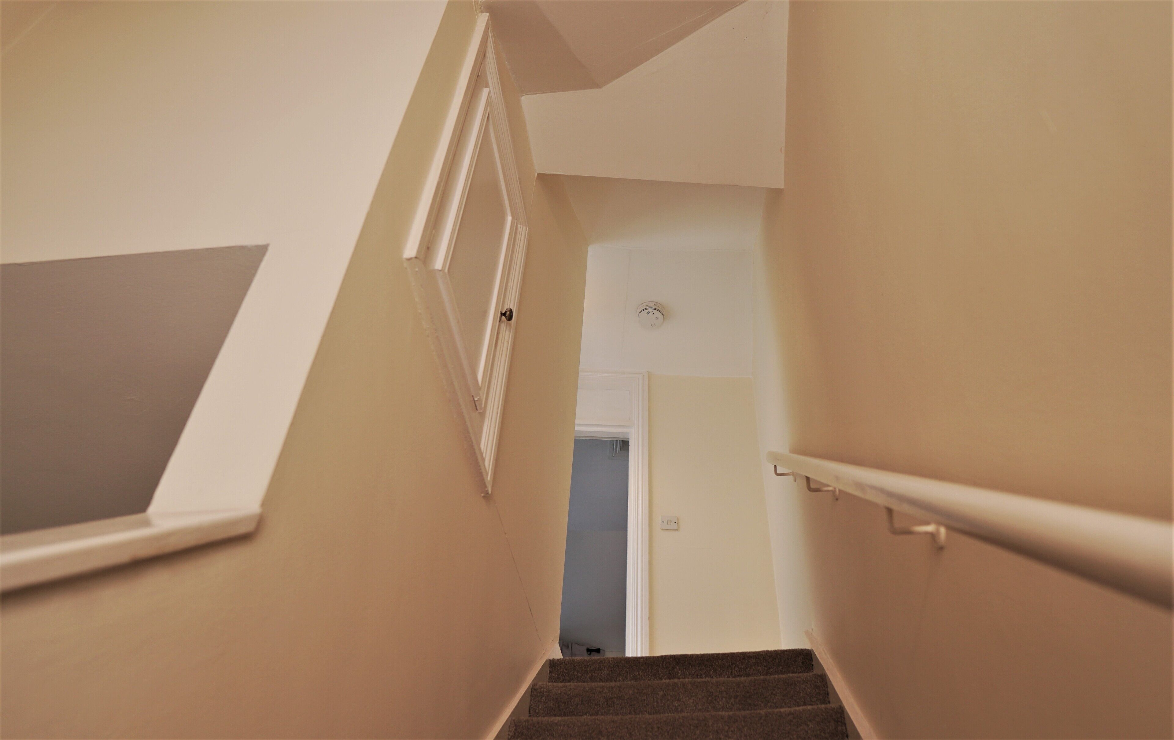 A staircase with a handrail, beige walls, and a door at the top.