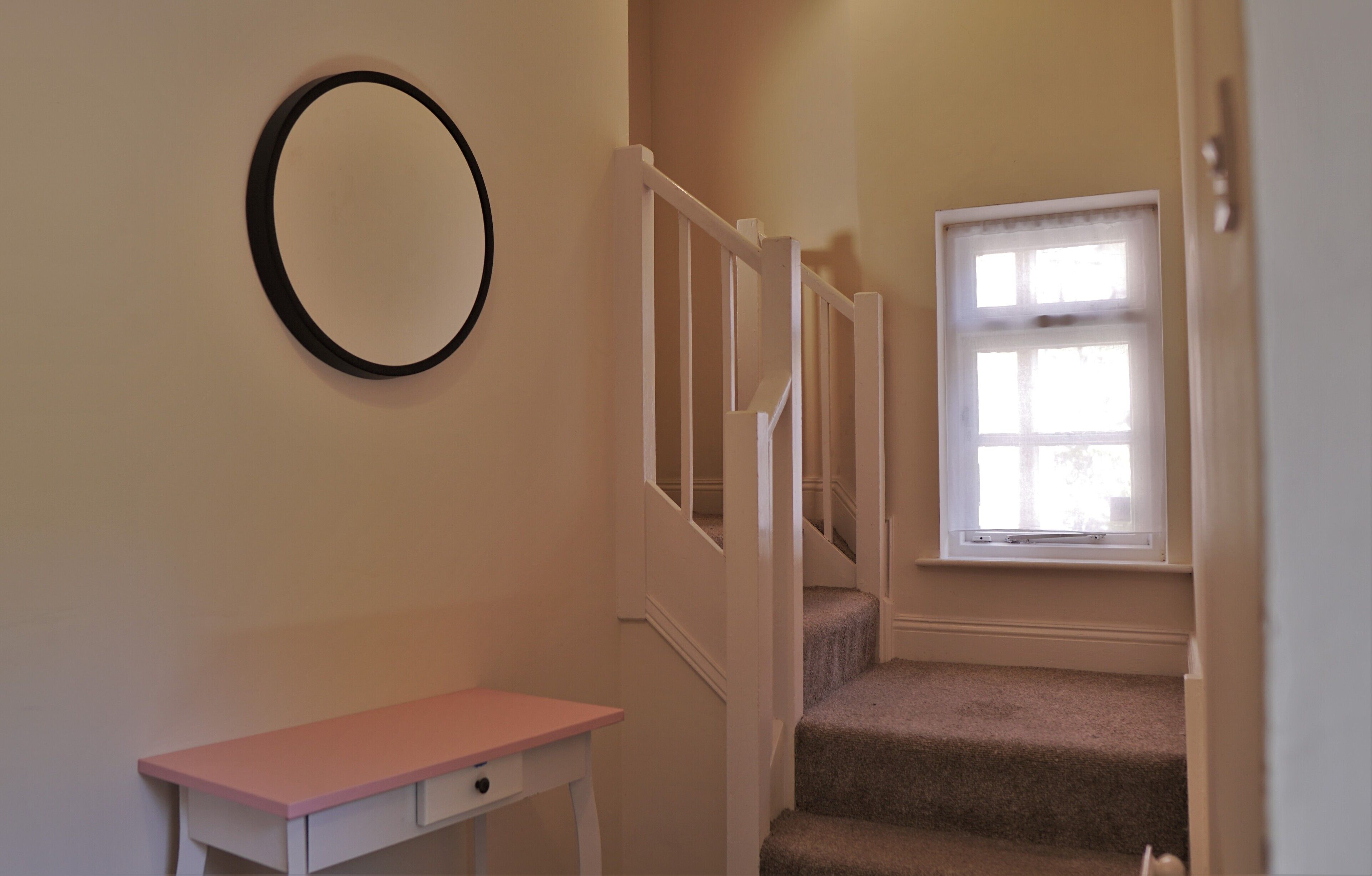 A staircase with a white railing, a small table with a drawer, and a window with blinds.