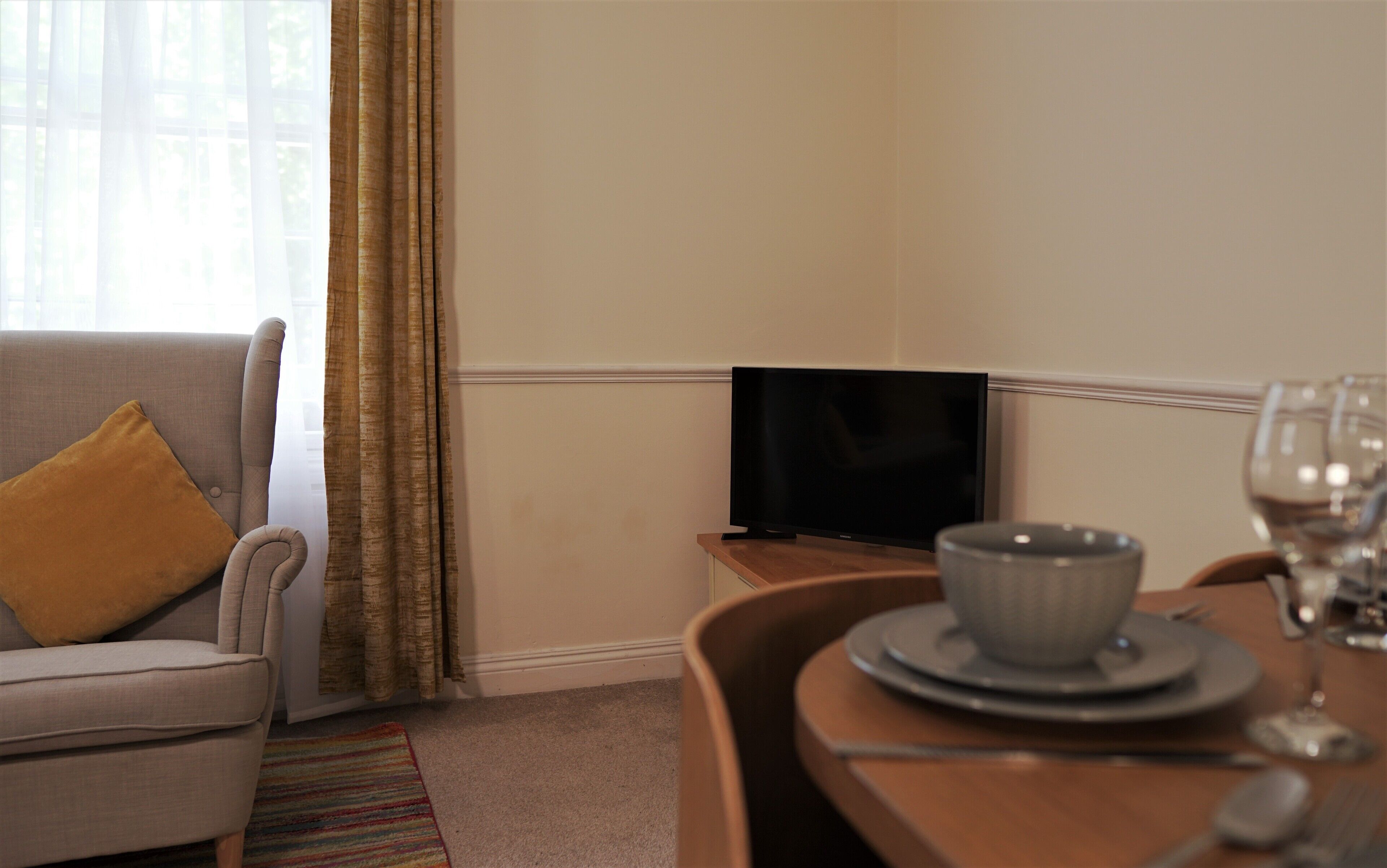 A hotel room with a sofa, a television, a dining table set with plates, a bowl, and a wine glass.