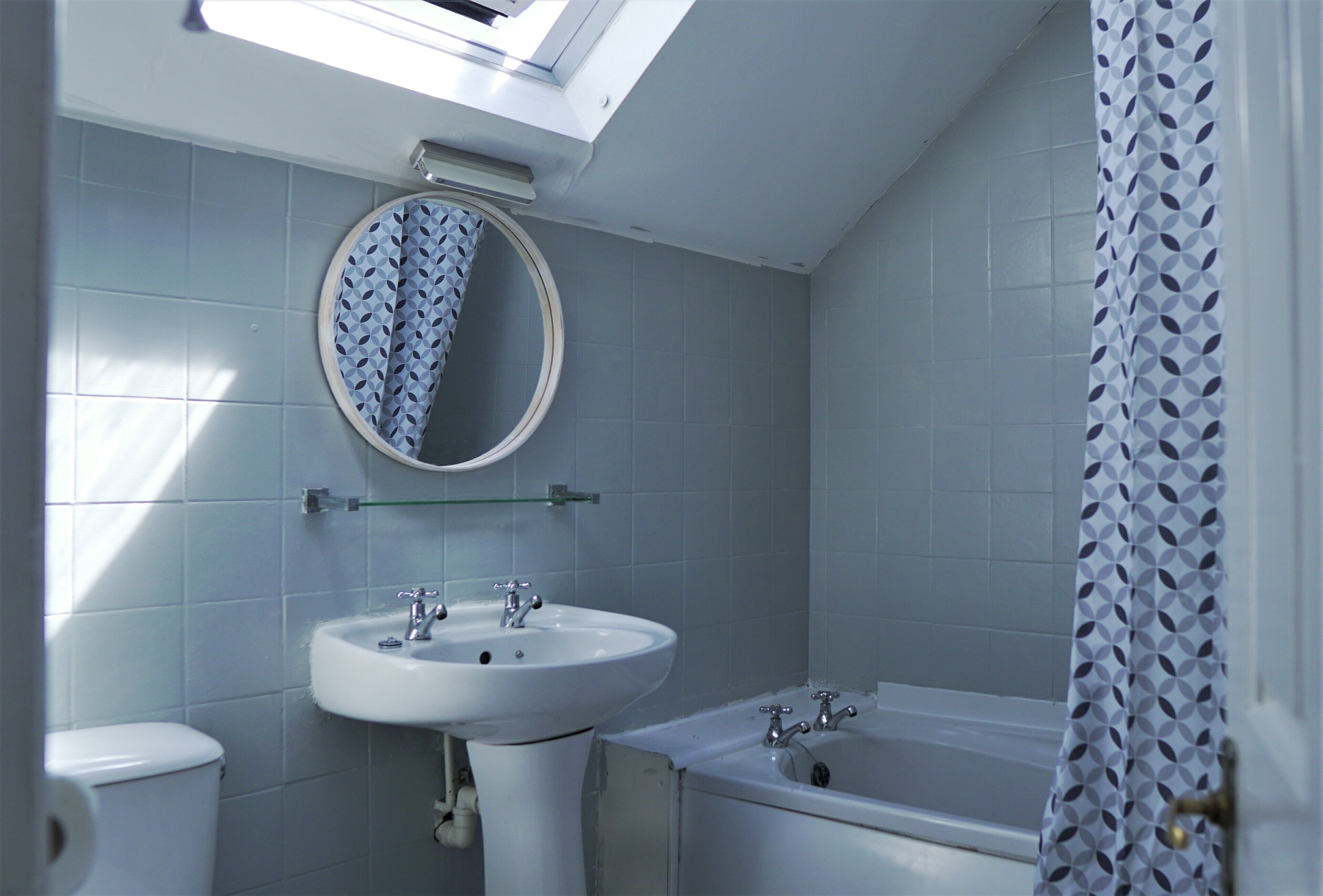 A bathroom with a skylight, a round mirror, a sink, a toilet, and a bathtub.