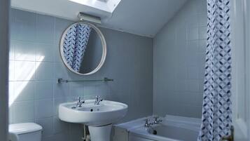 A bathroom with a skylight, a round mirror, a sink, a toilet, and a bathtub.