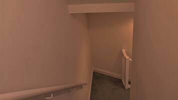 A narrow stairway with a handrail, carpeted steps, and white walls.