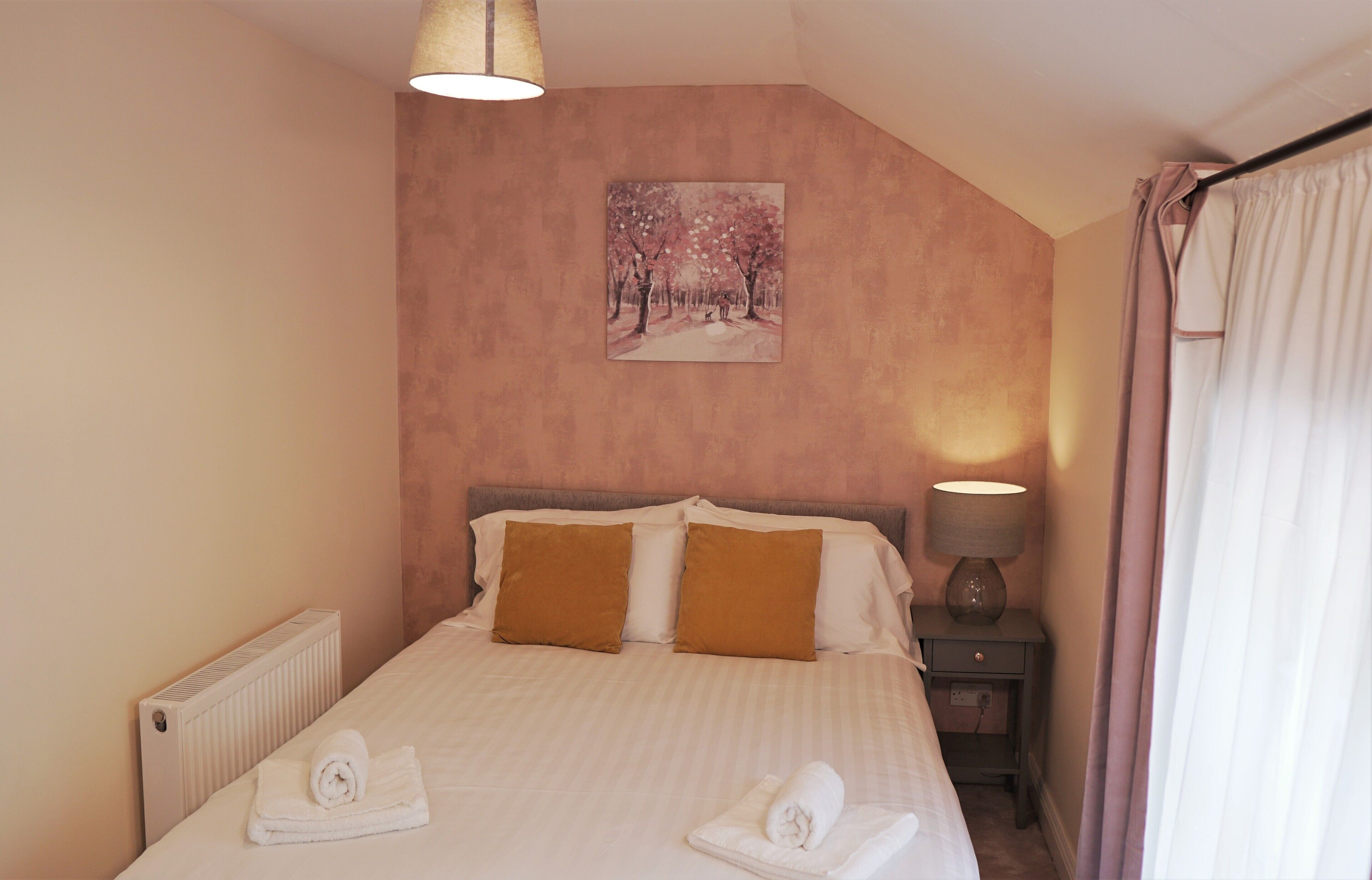 Un letto rifatto con due cuscini, una lampada da comodino e un quadro appeso al muro.