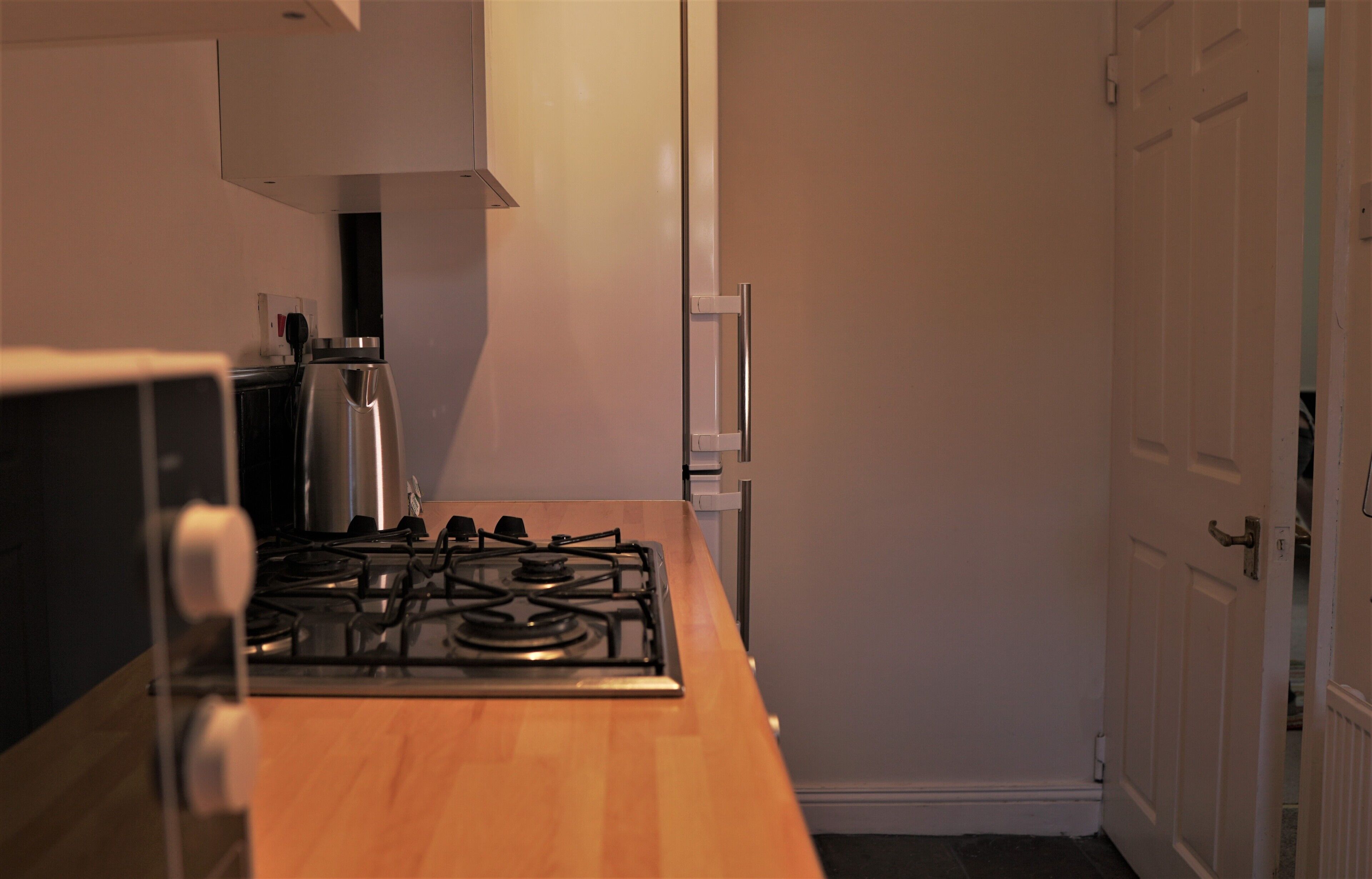 A compact kitchen with a gas stove, a kettle, and a white refrigerator.