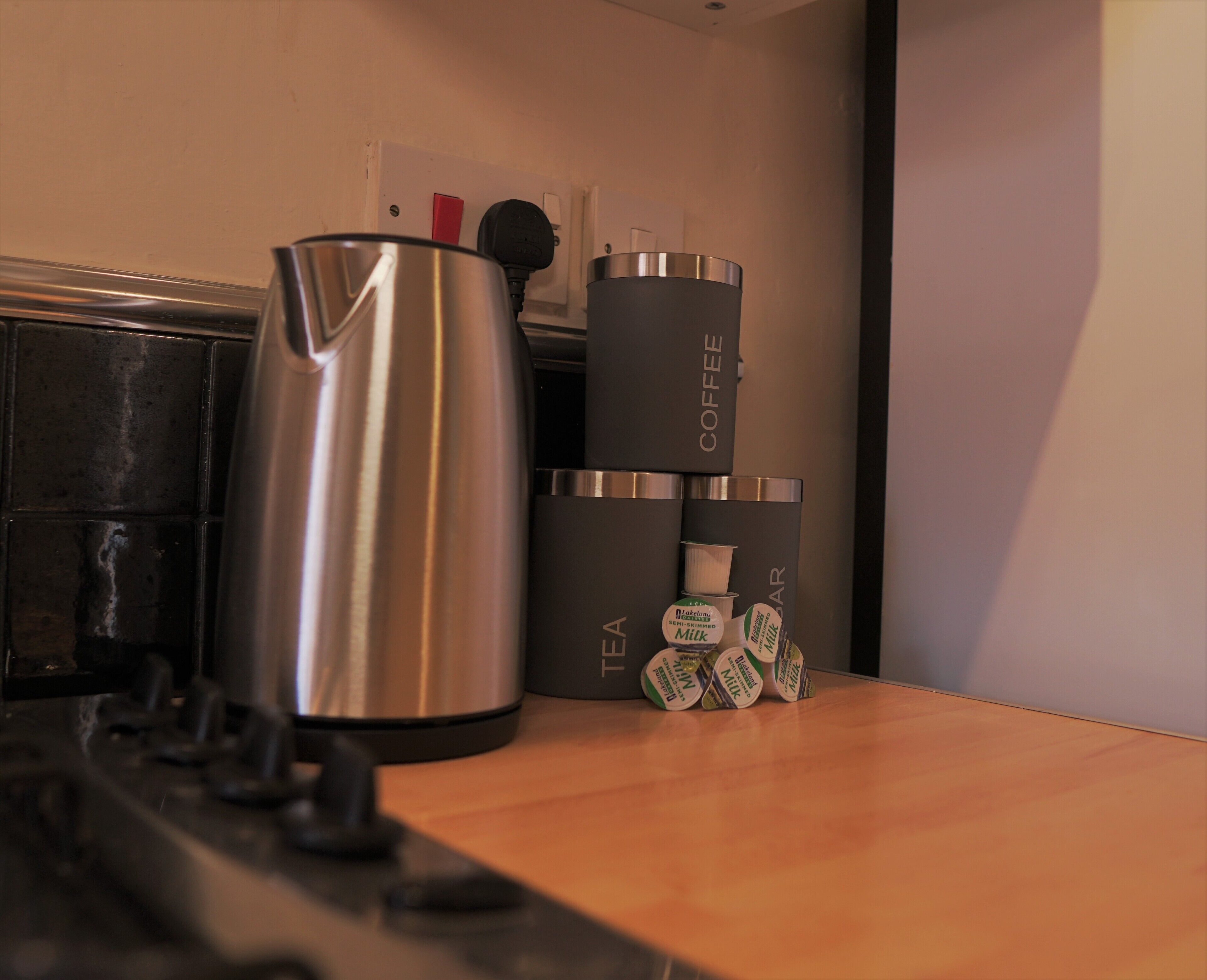 A kitchen counter with a stainless steel kettle, a coffee maker, and several containers labeled "TEA" and "COFFEE."