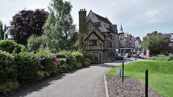 Un estrecho sendero empedrado que conduce a un edificio de estilo Tudor histórico con una torre destacada.
