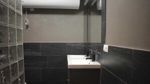 A bathroom with a white sink, dark tiles, and a glass shower enclosure. - Apartment (Cádiz)