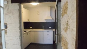 A kitchen with white cabinets, a black countertop, and a clock on the wall. - Apartment (Cádiz)