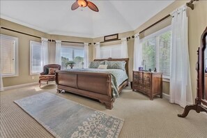Quarto com uma cama grande, penteadeira de madeira, mesa de cabeceira e ventilador de teto.