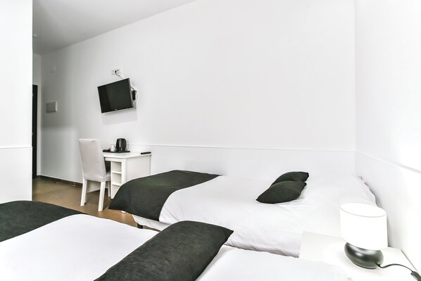 A hotel room with two beds, a desk, a chair, a TV, and a bedside lamp.