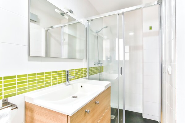 Un baño moderno con un lavamanos blanco, tocador de madera y cabina de ducha de vidrio.