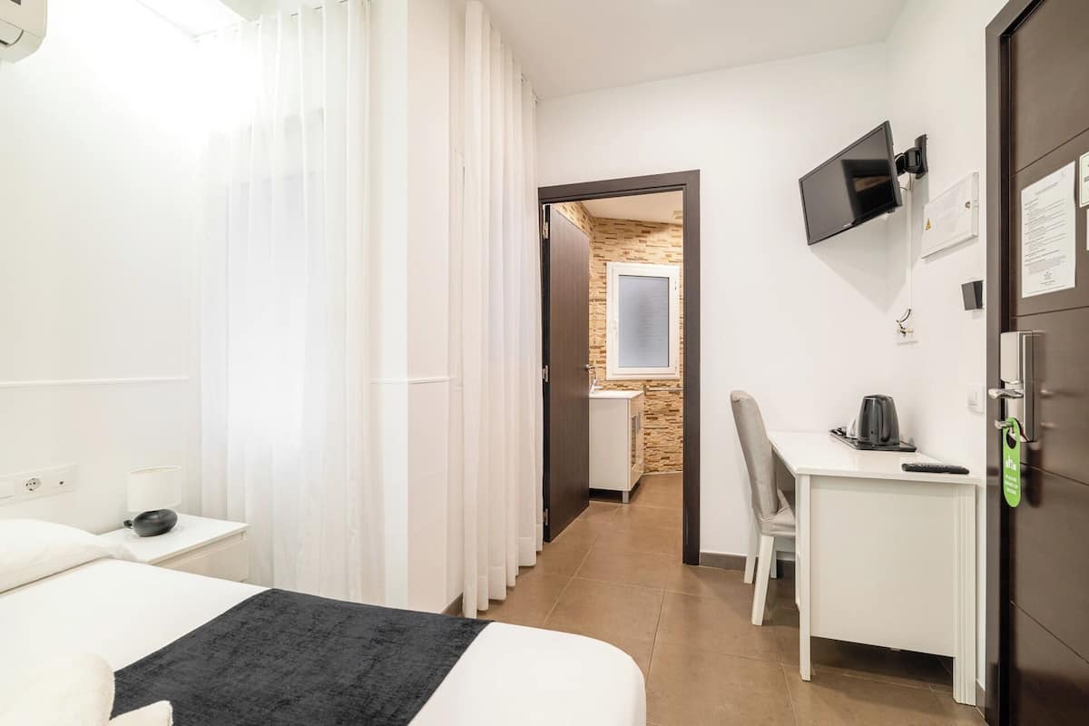 Habitación de hotel con cama, escritorio, silla, televisor y baño visible a través de una puerta abierta.