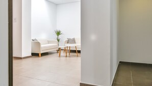 Un área de espera moderna y minimalista con un sofá blanco, una mesita y una planta en maceta.