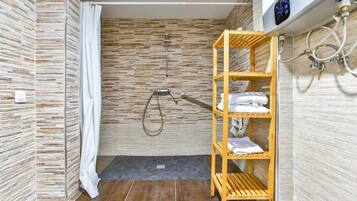 A modern shower area with a wooden shelf holding towels, a showerhead, and a control panel.